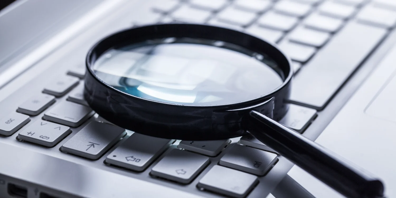 Magnifying glass resting on a laptop keyboard, representing searching for answers online